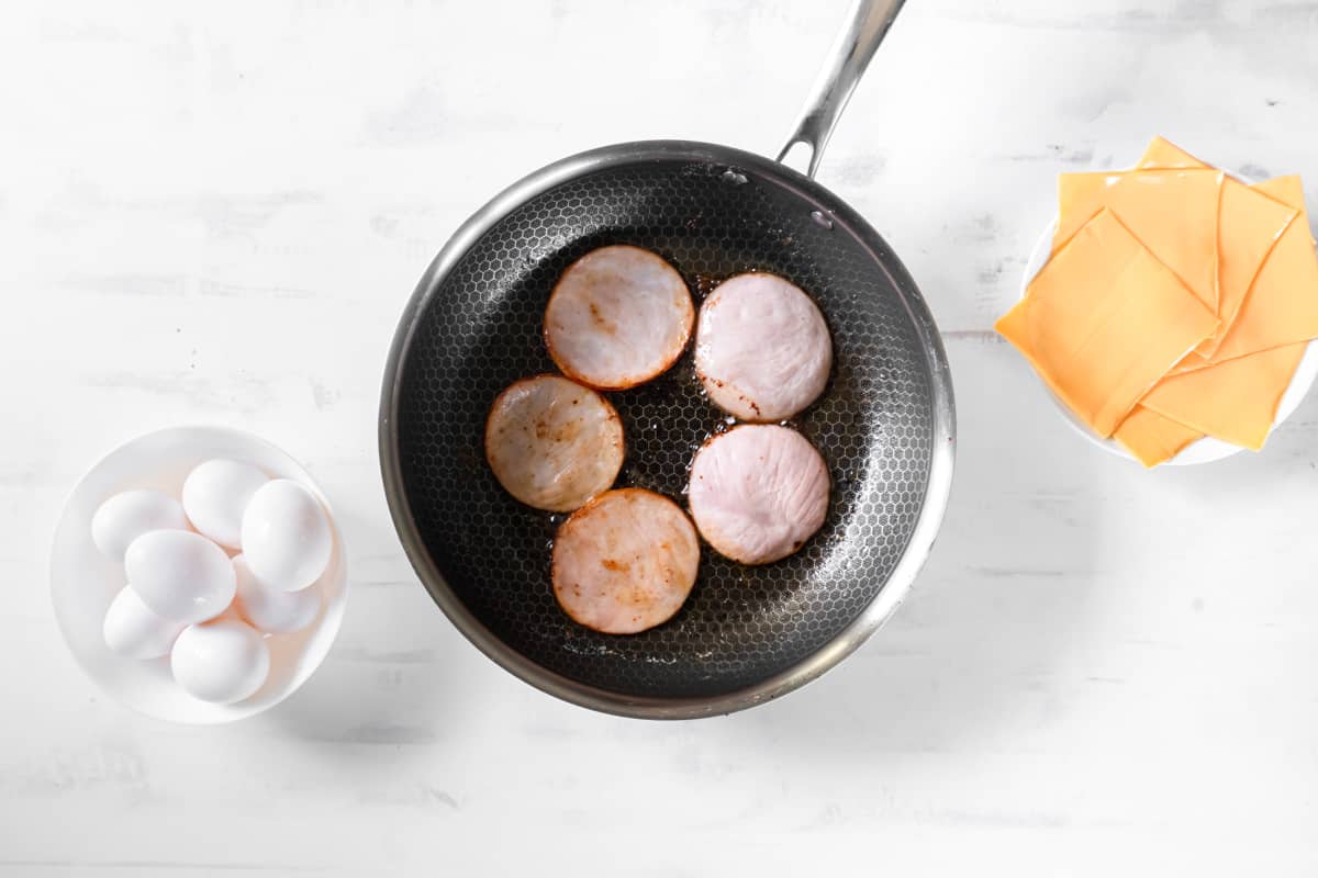 5 pieces of canadian bacon in a skillet.