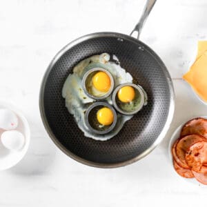 3 eggs cooking in egg rings a skillet.