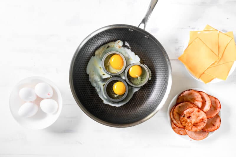 3 eggs cooking in egg rings a skillet.