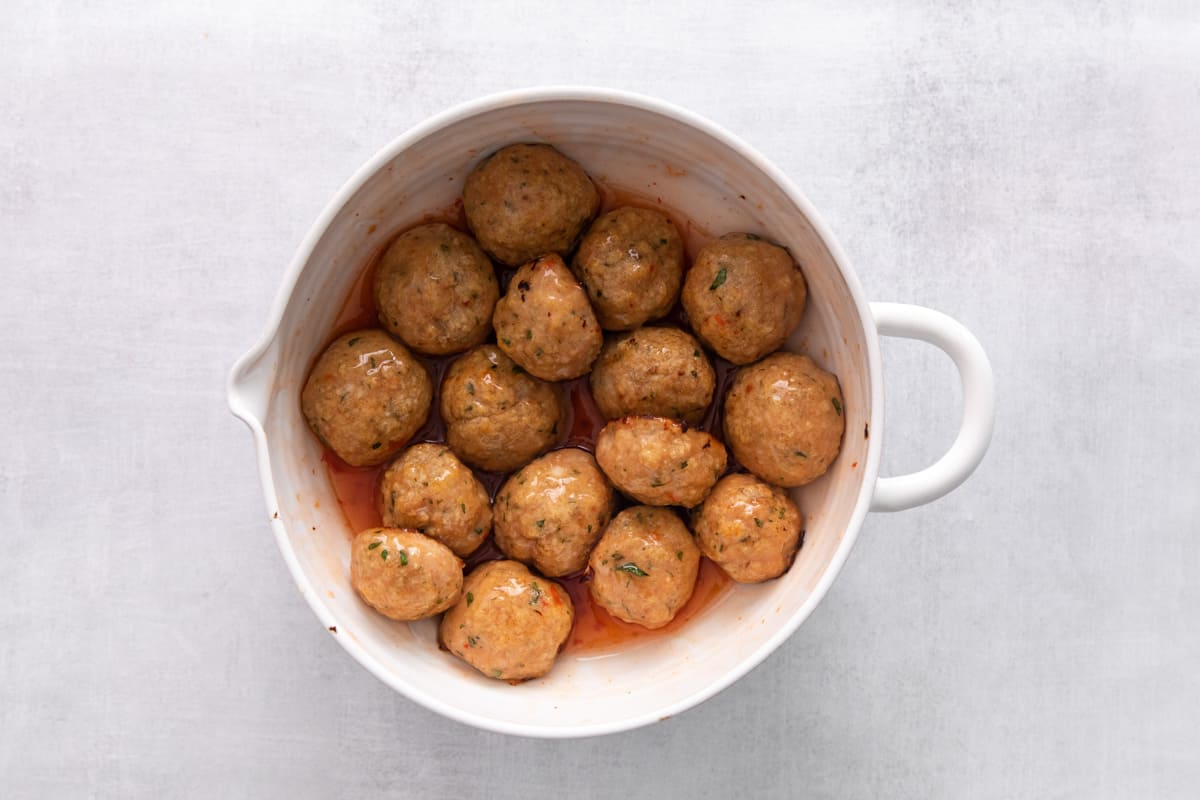 Chicken meatballs in a mixing bowl, tossed in sweet chili sauce.