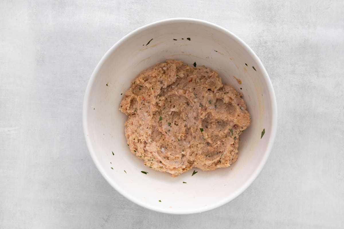 Ground chicken meatball mixture in a white bowl.