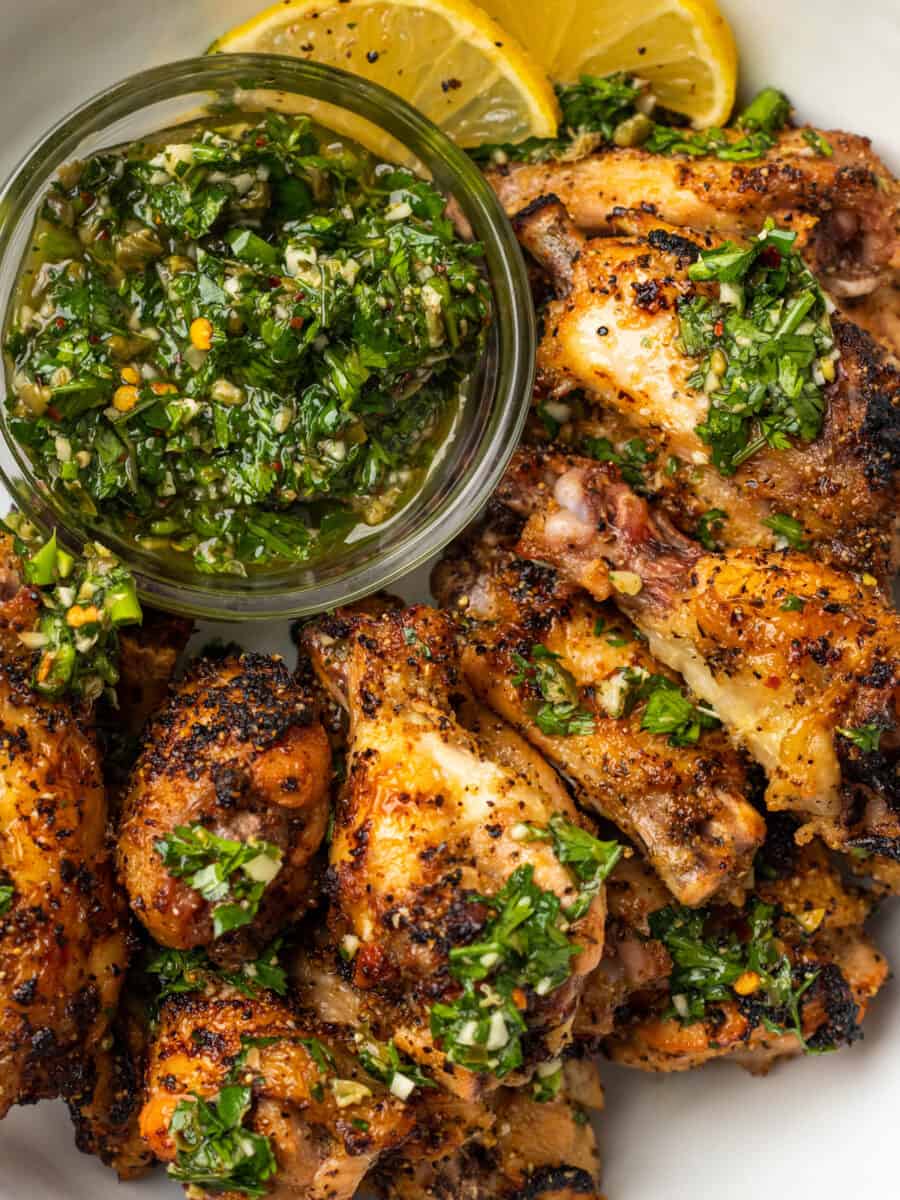 lemon pepper wings on a platter with gremolata in a glass bowl.
