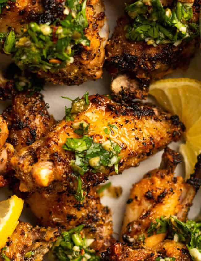 close up of lemon pepper wings with gremolata and lemon wedges.