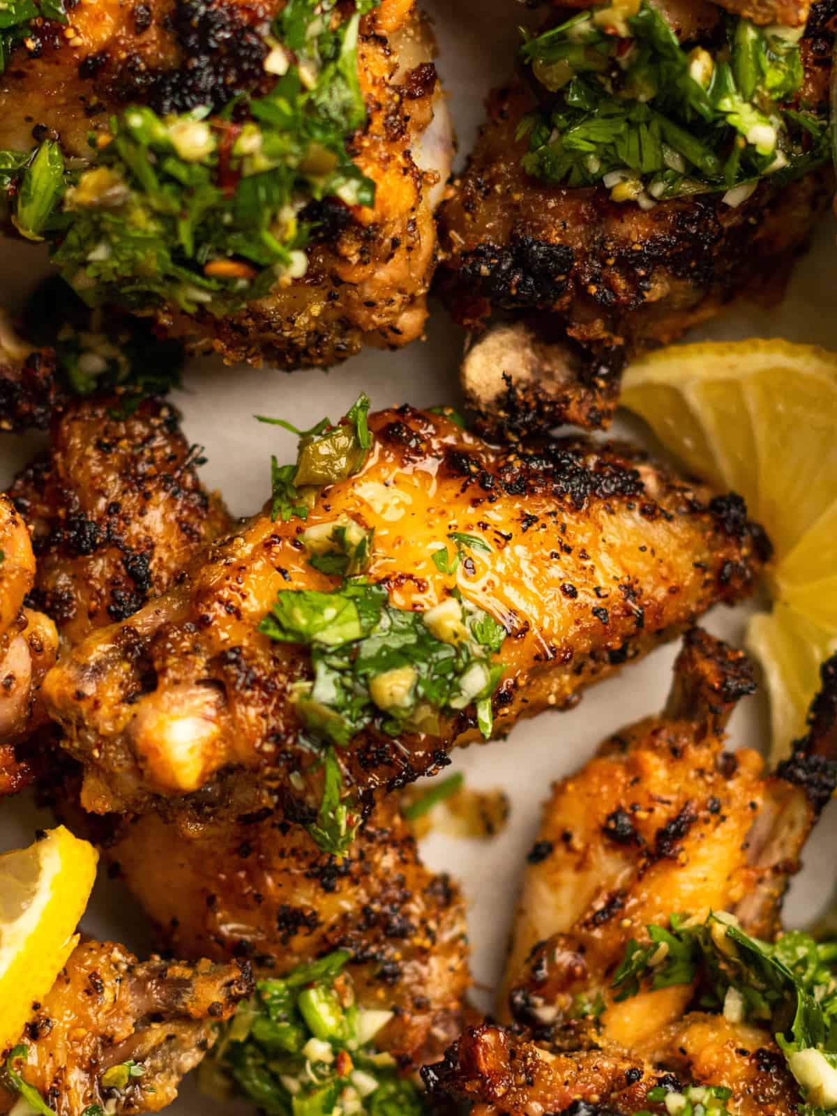 close up of lemon pepper wings with gremolata and lemon wedges.