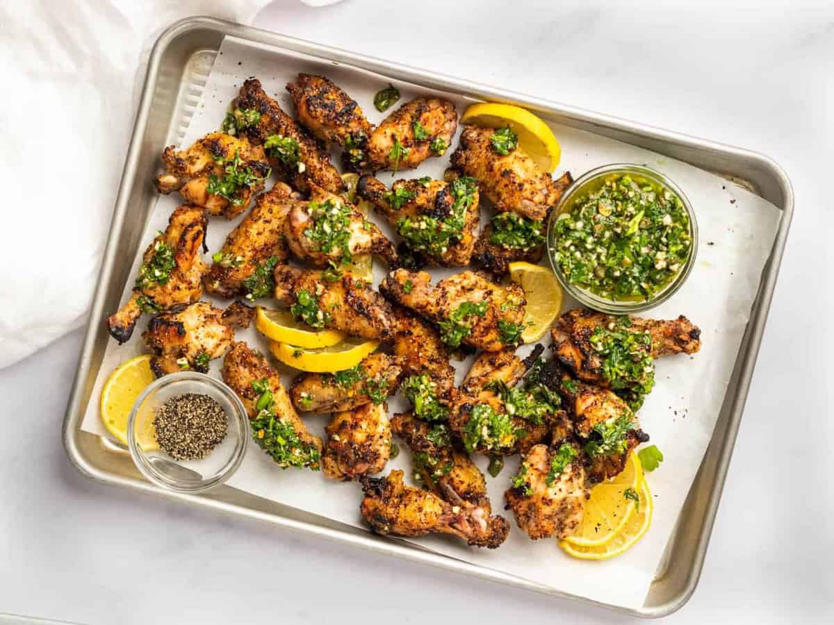 overhead view of lemon pepper wings on a baking sheet with gremolata and lemon wedges.