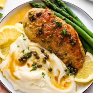 a serving of stuffed chicken piccata on a plate with mashed potatoes, asparagus, and lemon slices.