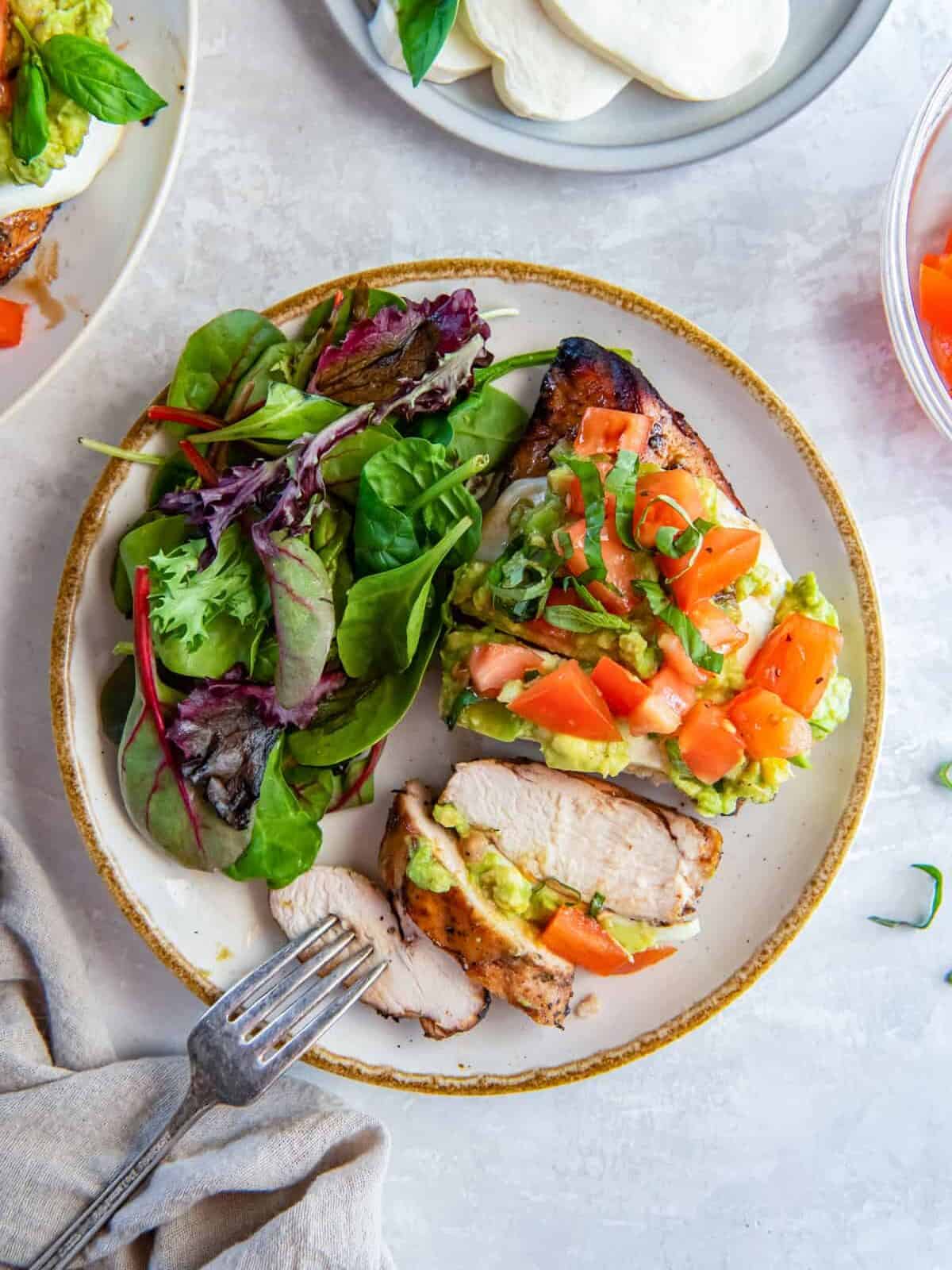 overhead view of a sliced california grilled chicken breast on a white plate with a salad and a fork.