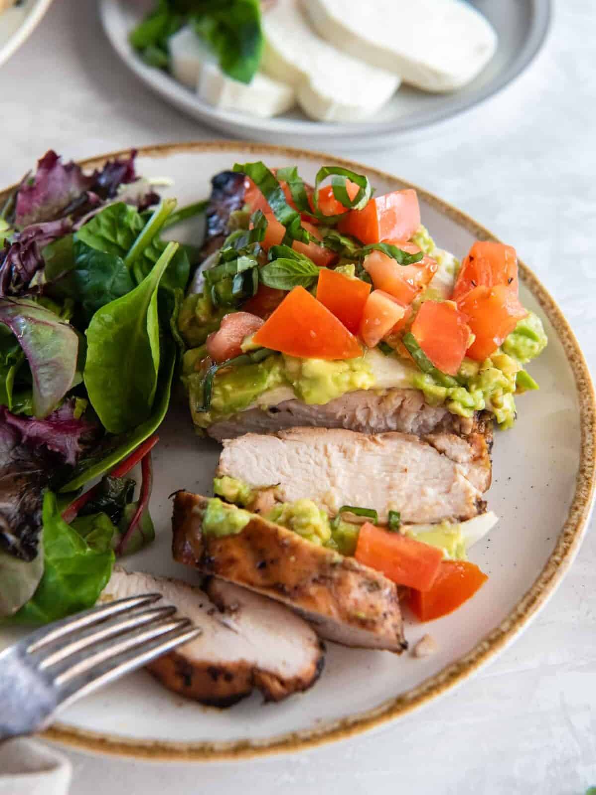 three-quarters view of a sliced california grilled chicken breast on a white plate with a salad and a fork.