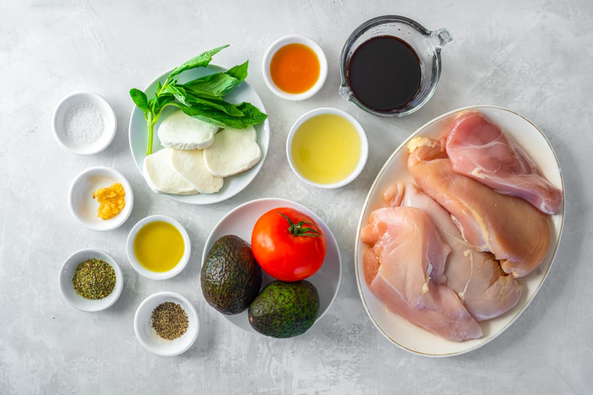 overhead view of ingredients for california grilled chicken: chicken breast, avocado, tomatoes, balsamic marinade, mozzarella.
