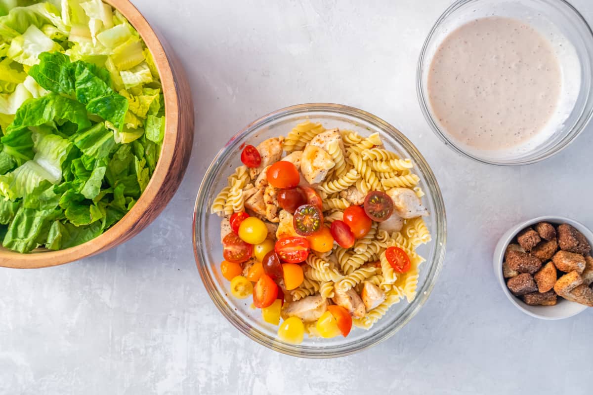 Tomatoes and chicken added to cooked pasta in a glass bowl.