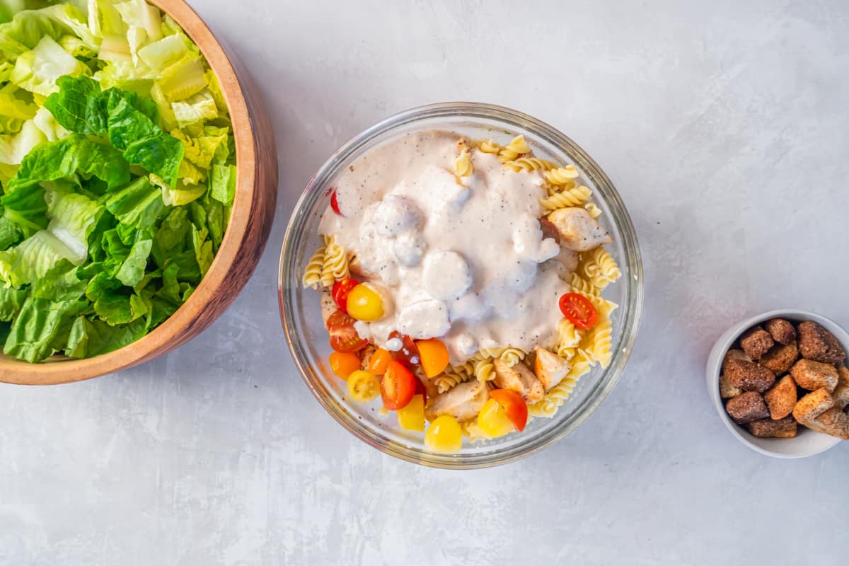 Caesar dressing added to a bowl of pasta.