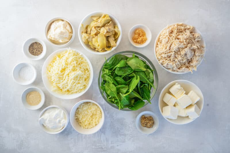 overhead view of ingredients for spinach artichoke chicken casserole in individual bowls.