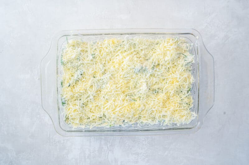 cheese sprinkled over spinach artichoke chicken casserole in a glass rectangular baking pan.