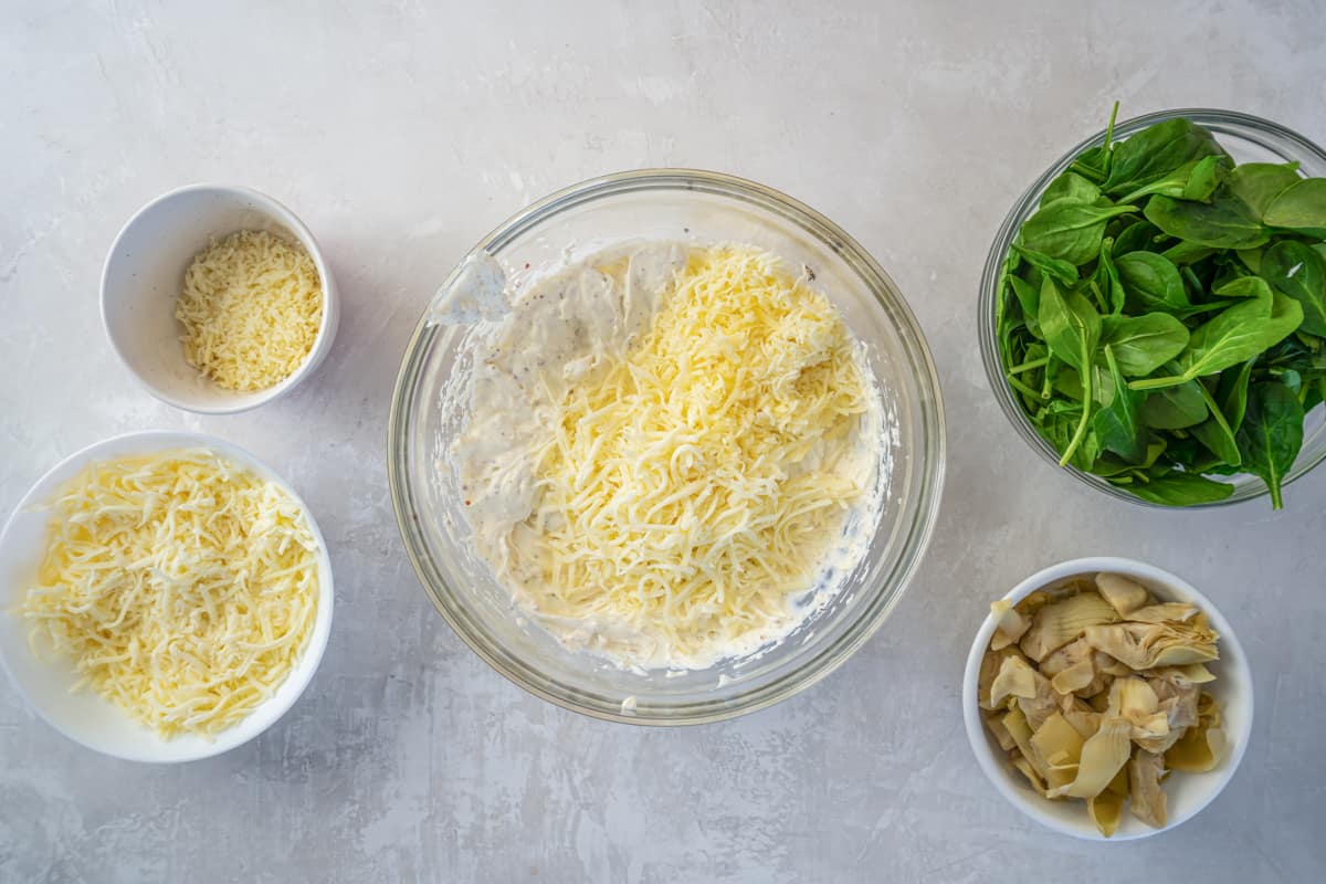 cheese added to cream cheese mixture in a glass bowl.