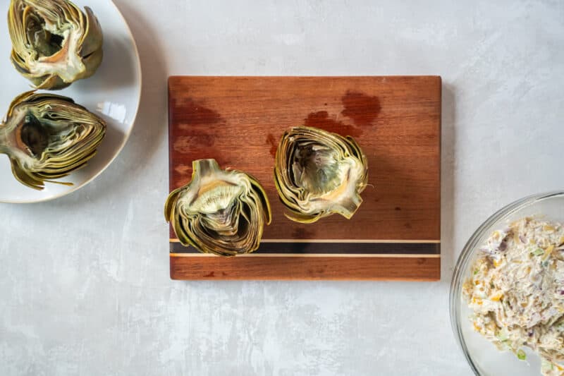 a halved and cored artichoke on a wooden cutting board.
