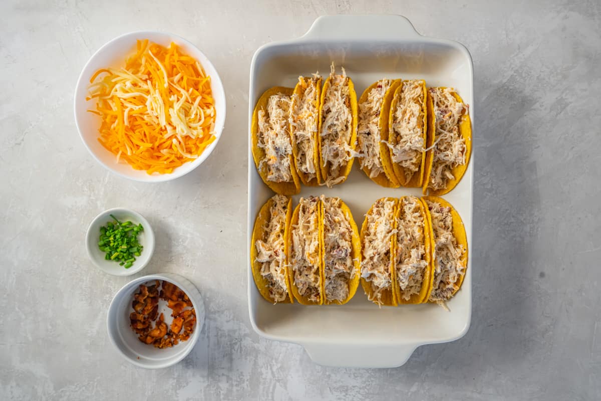 crack chicken mixture added to taco shells standing up in a white rectangular baking pan.