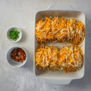 cheese sprinkled over crack chicken tacos in a rectangular white baking pan.
