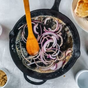 sautéed onions in a cast iron skillet with a wooden spoon.