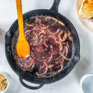 wine added to sautéed onions in a cast iron skillet with a wooden spoon.