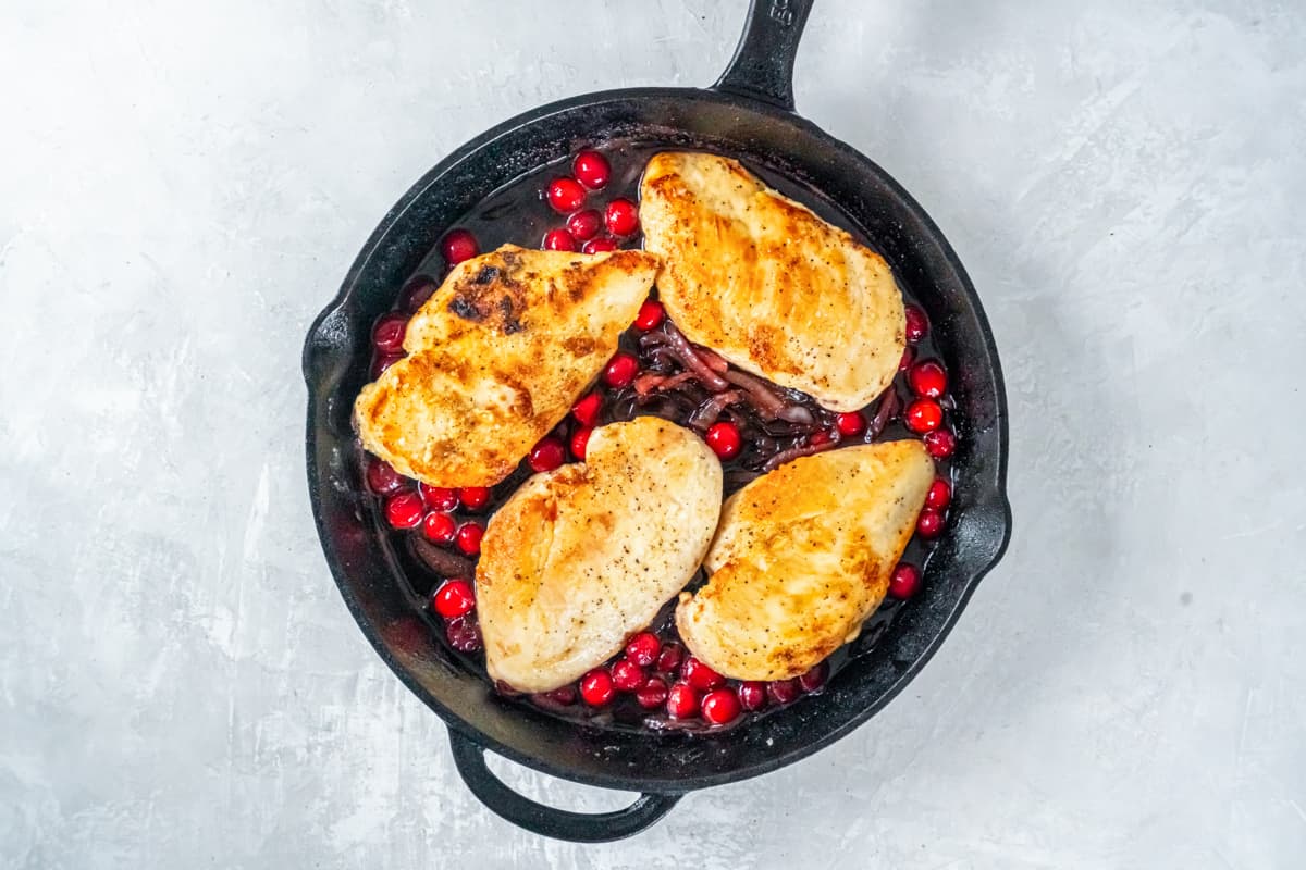 chicken added to sautéed onions and cranberries in a cast iron skillet.