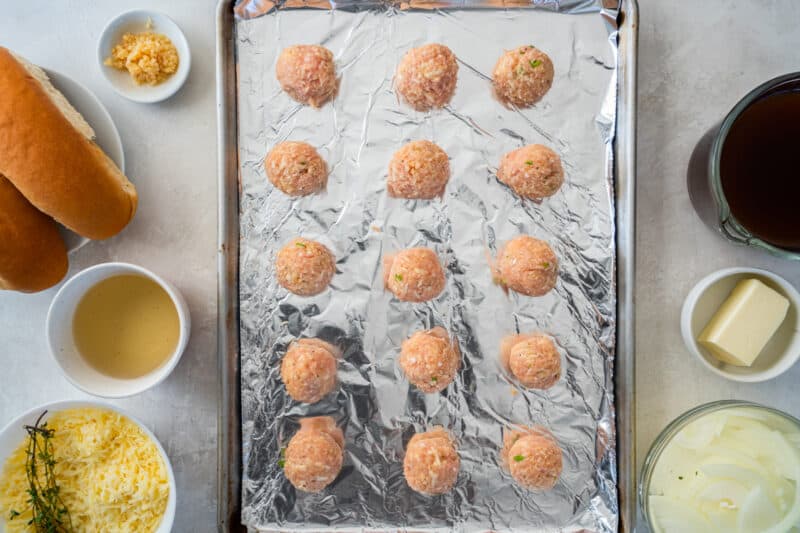 15 french onion chicken meatballs on a foil lined baking sheet.