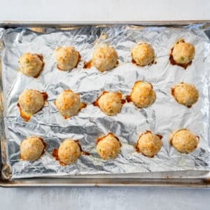 15 baked french onion chicken meatballs on a foil lined baking sheet.