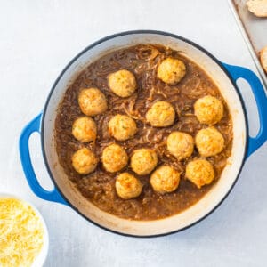 meatballs added to french onion soup in a blue and white dutch oven.