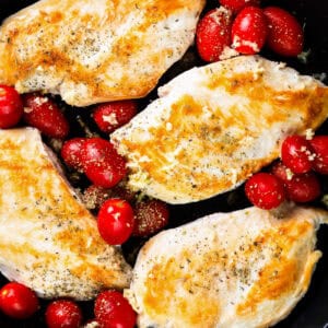 seared chicken breasts in a skillet with grape tomatoes.