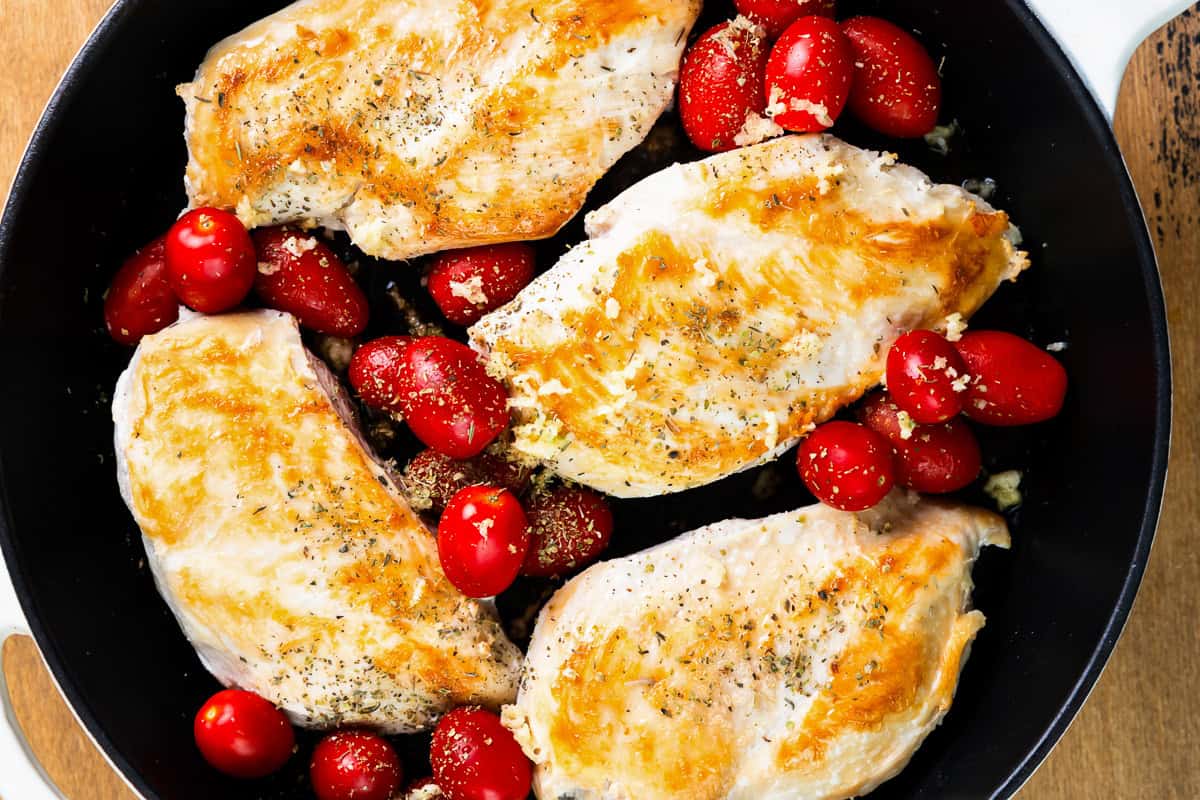 seared chicken breasts in a skillet with grape tomatoes.