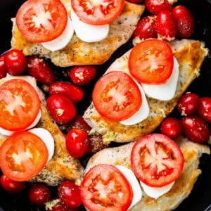 seared chicken breasts topped with cheese and tomato slices in a skillet with grape tomatoes.