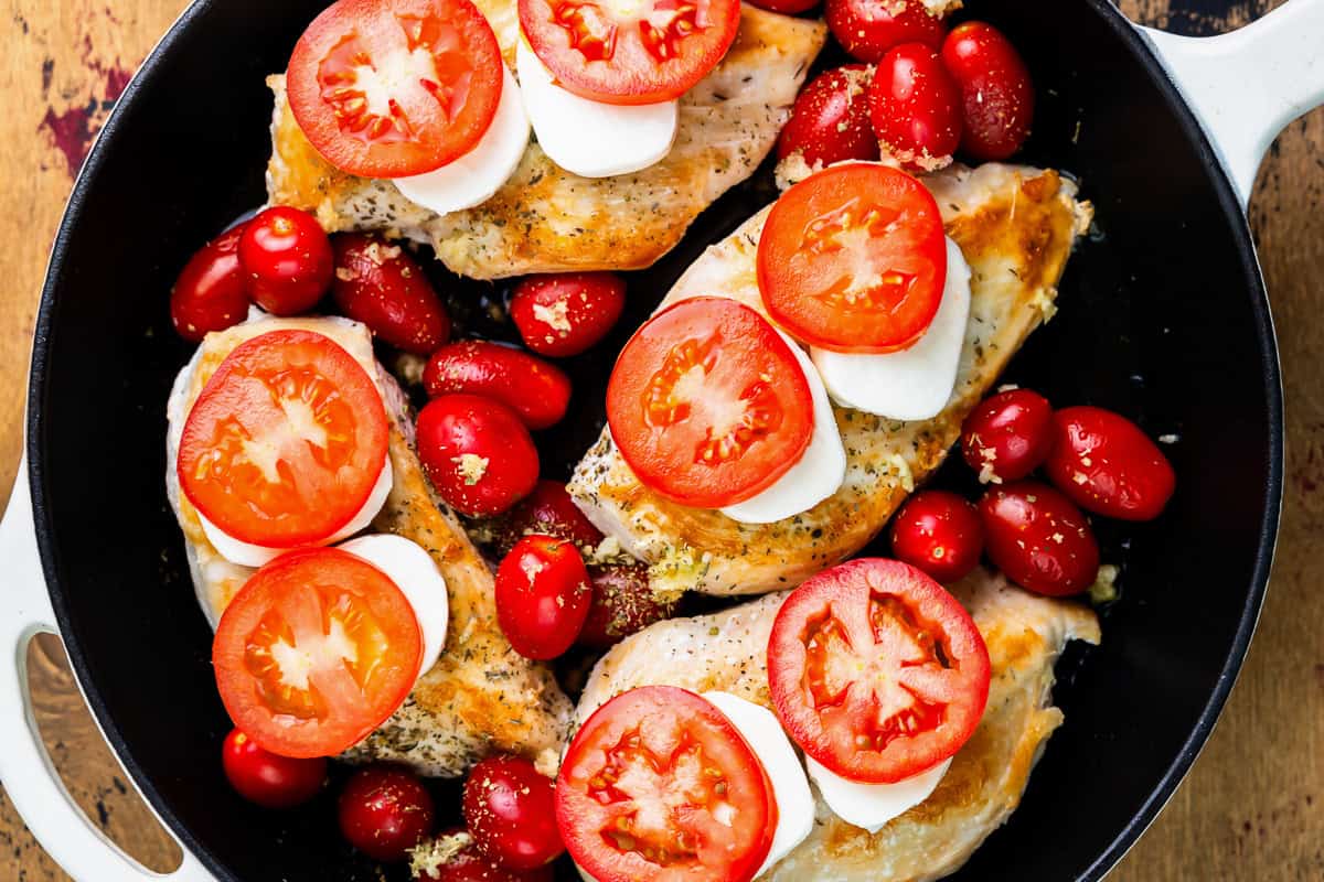 seared chicken breasts topped with cheese and tomato slices in a skillet with grape tomatoes.