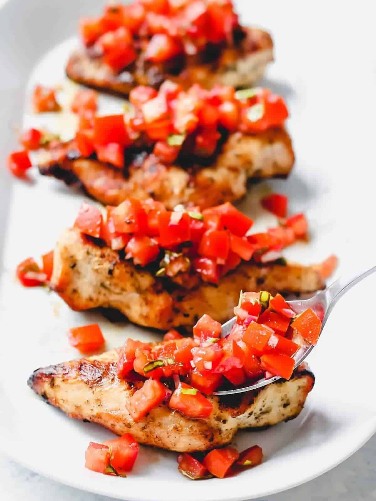 grilled chicken breasts with bruschetta topping on a serving plate