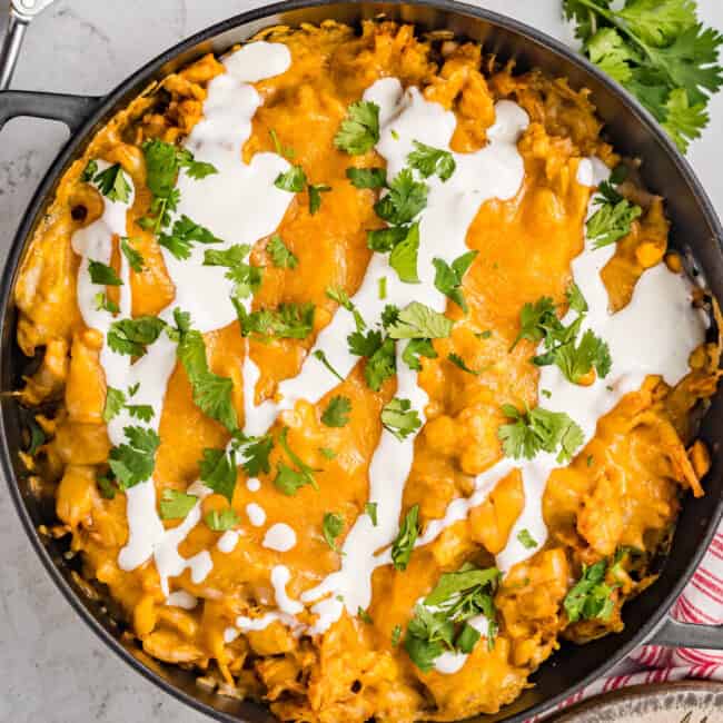 cheesy chicken nachos in a skillet with sour cream and cilantro.