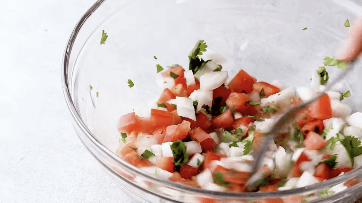 Salsa is being mixed in a glass bowl. 
