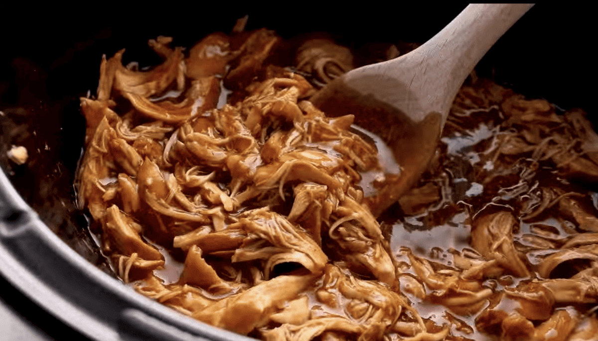 Shredded bbq chicken is being mixed in a Crockpot.