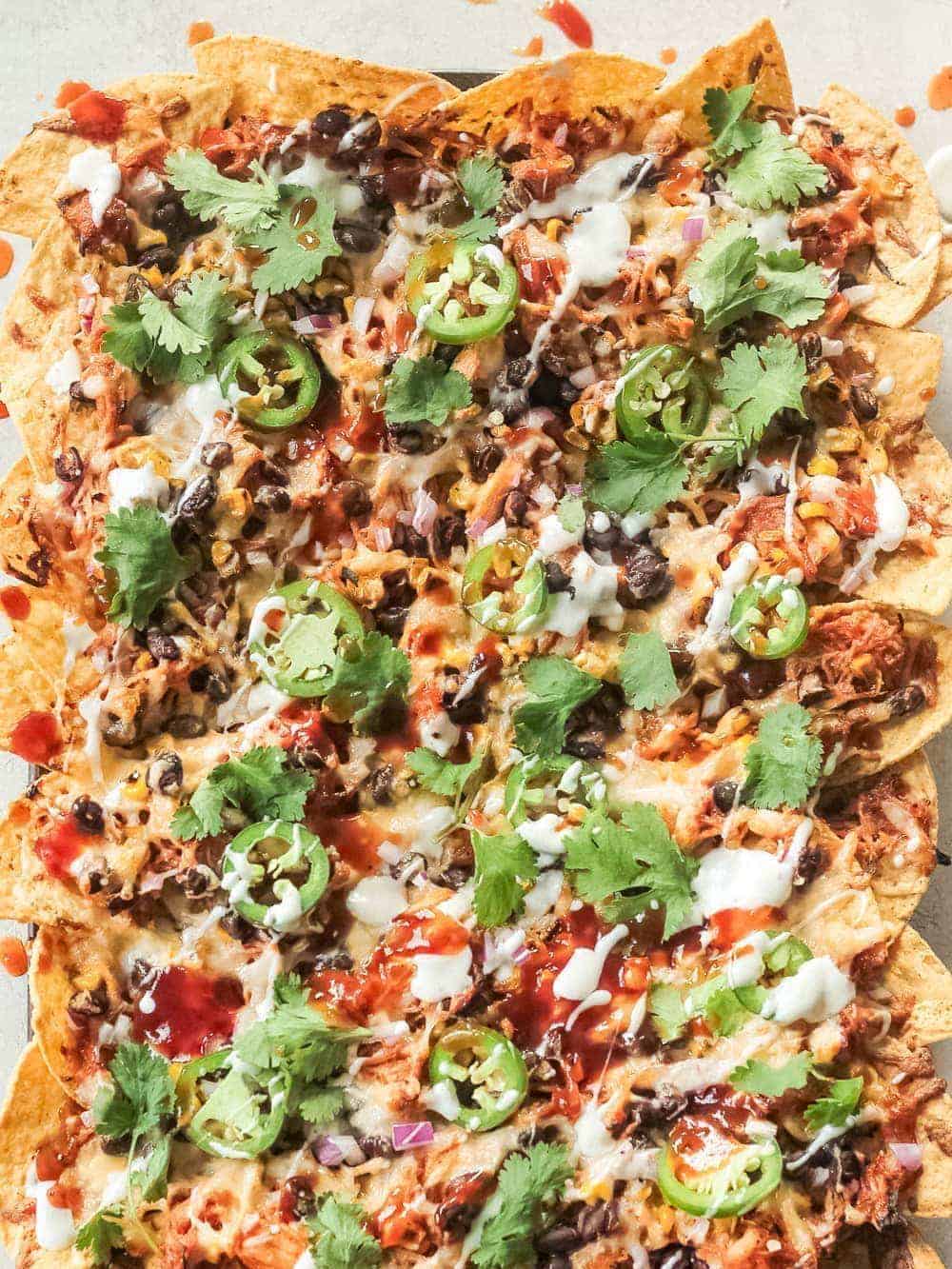 baked nachos topped with bbq chicken, jalapeños, corn, black beans, and more ingredients 