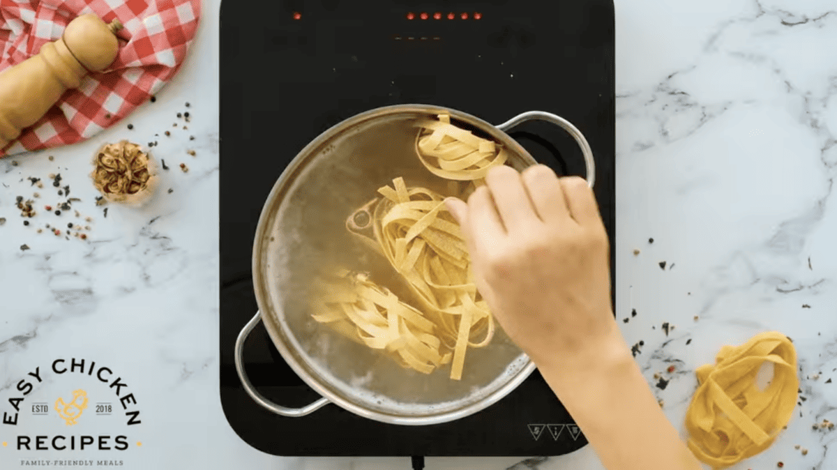 A person preparing chicken alfredo from scratch by pouring pasta into a pan on a stove.