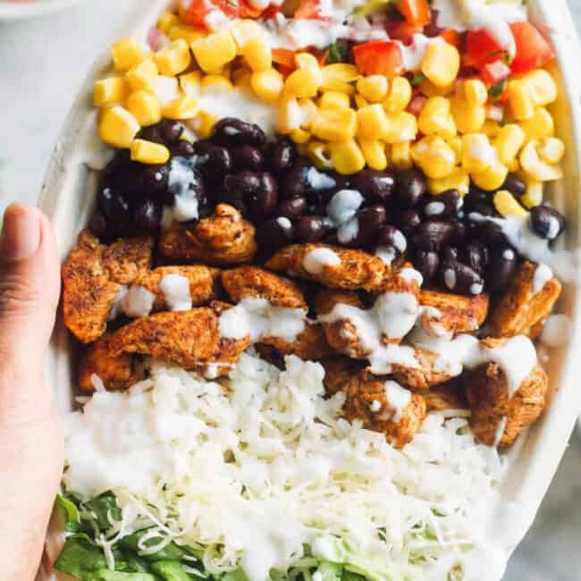 A hand holding a bowl of Copycat Chipotle Chicken salad.