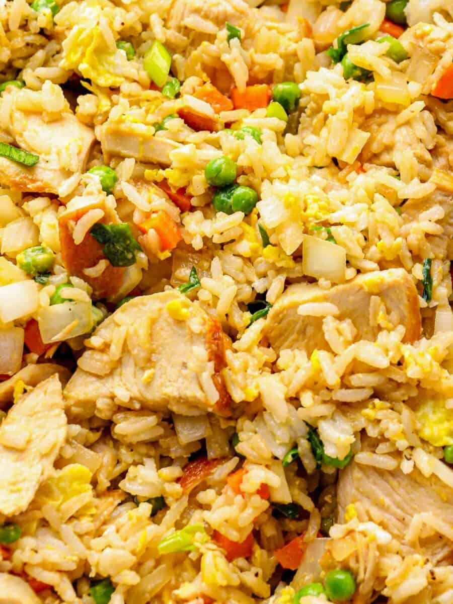 Close up on fried rice with chicken, peas, carrots, onions, and egg.