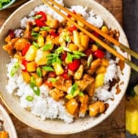 overhead view of a bowl of pineapple chicken over rice with chopsticks.