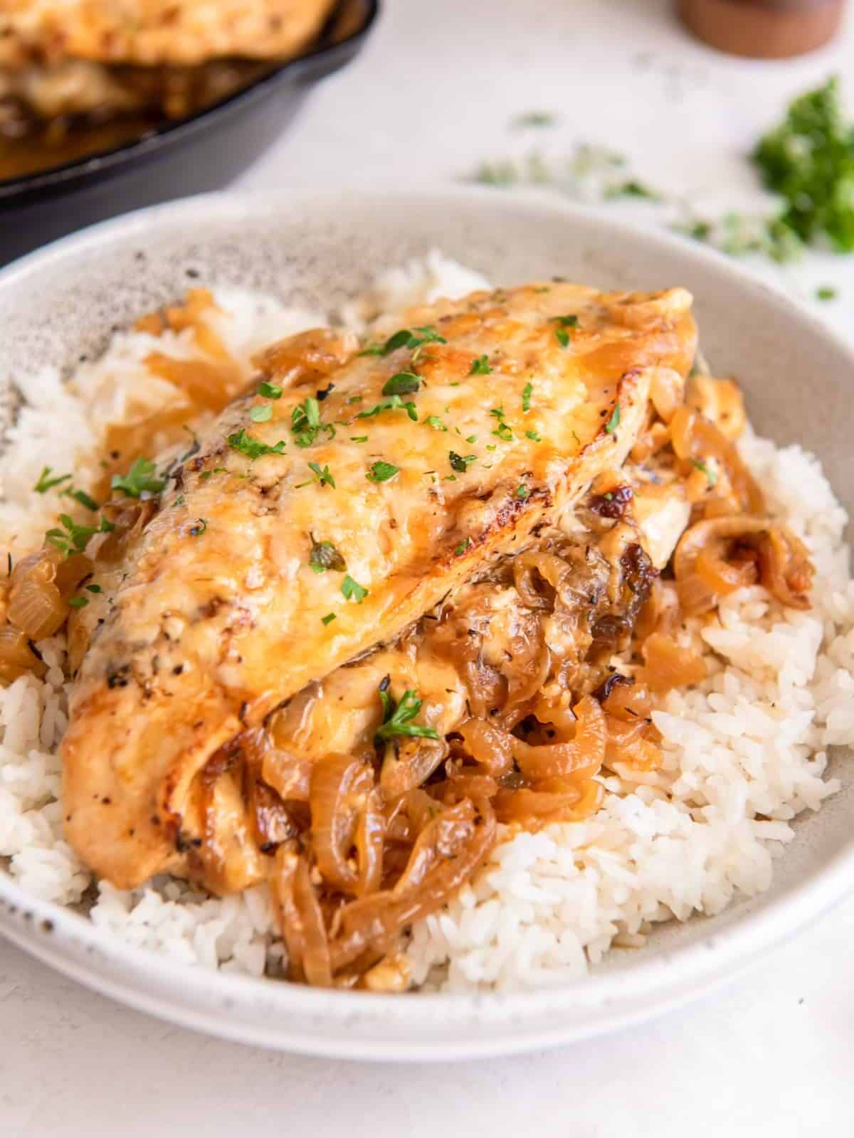 french onion stuffed chicken breast on a bed of white rice in a white bowl.