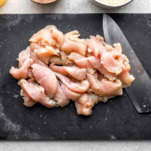 chopped chicken on a black cutting board with a knife.