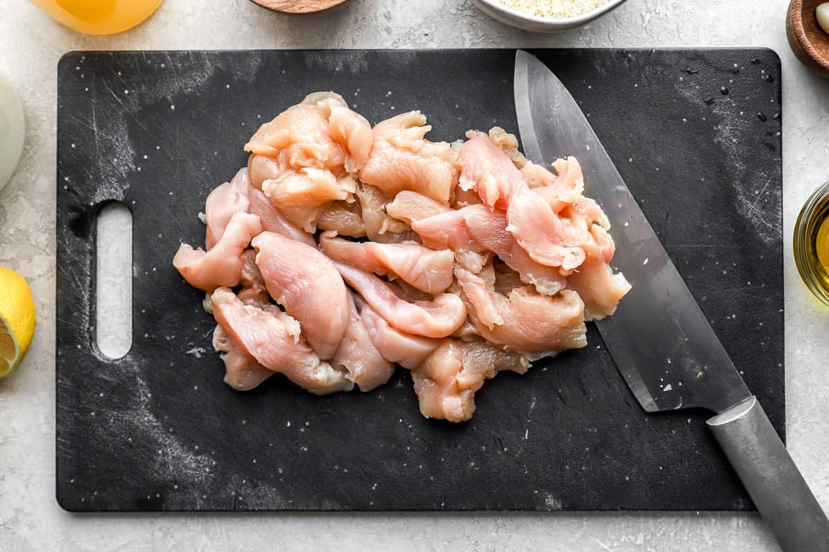 chopped chicken on a black cutting board with a knife.