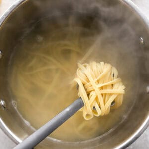 lifting a scoop of boiled fettuccine pasta from a pot.