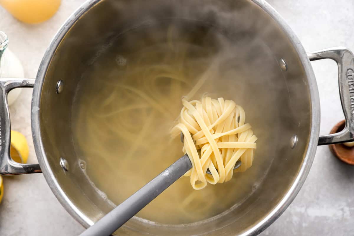 lifting a scoop of boiled fettuccine pasta from a pot.