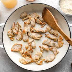 cooking chicken slices in a pan with a wooden spatula.