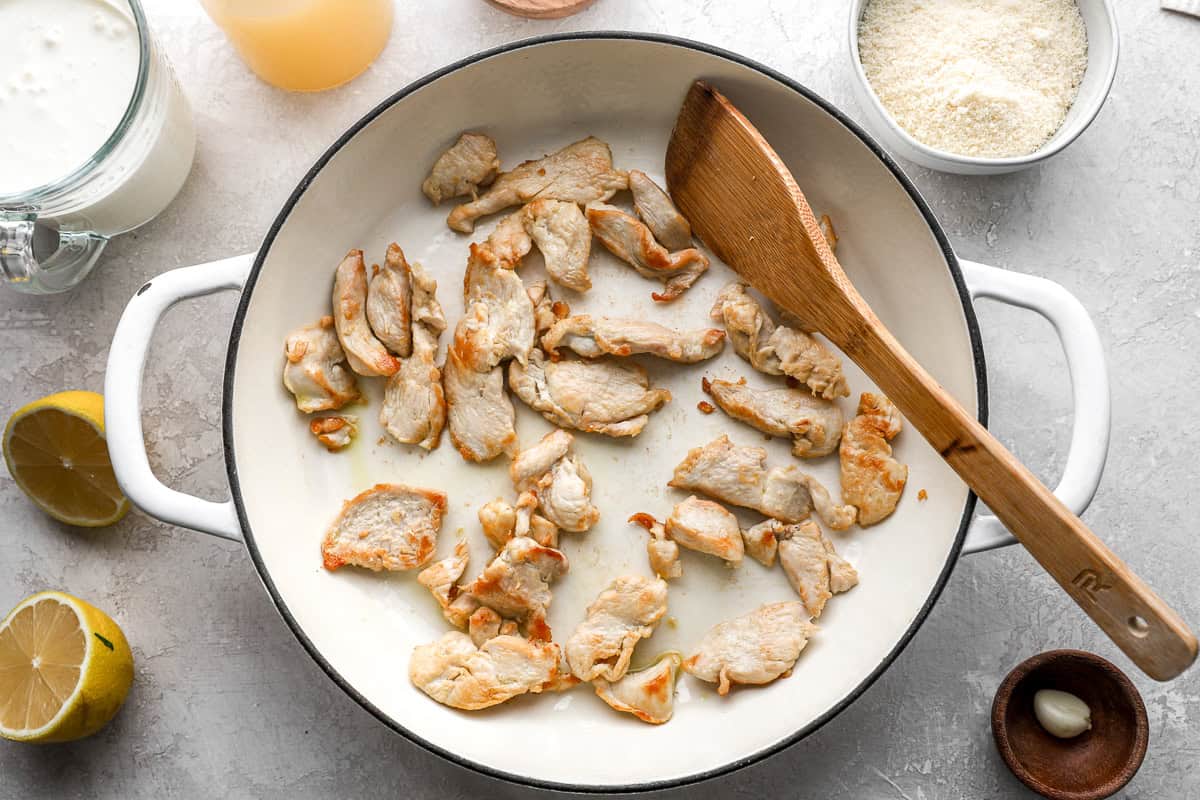 cooking chicken slices in a pan with a wooden spatula.