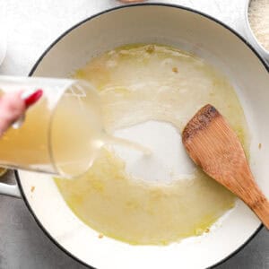 pouring chicken broth into a pan with a wooden spatula.