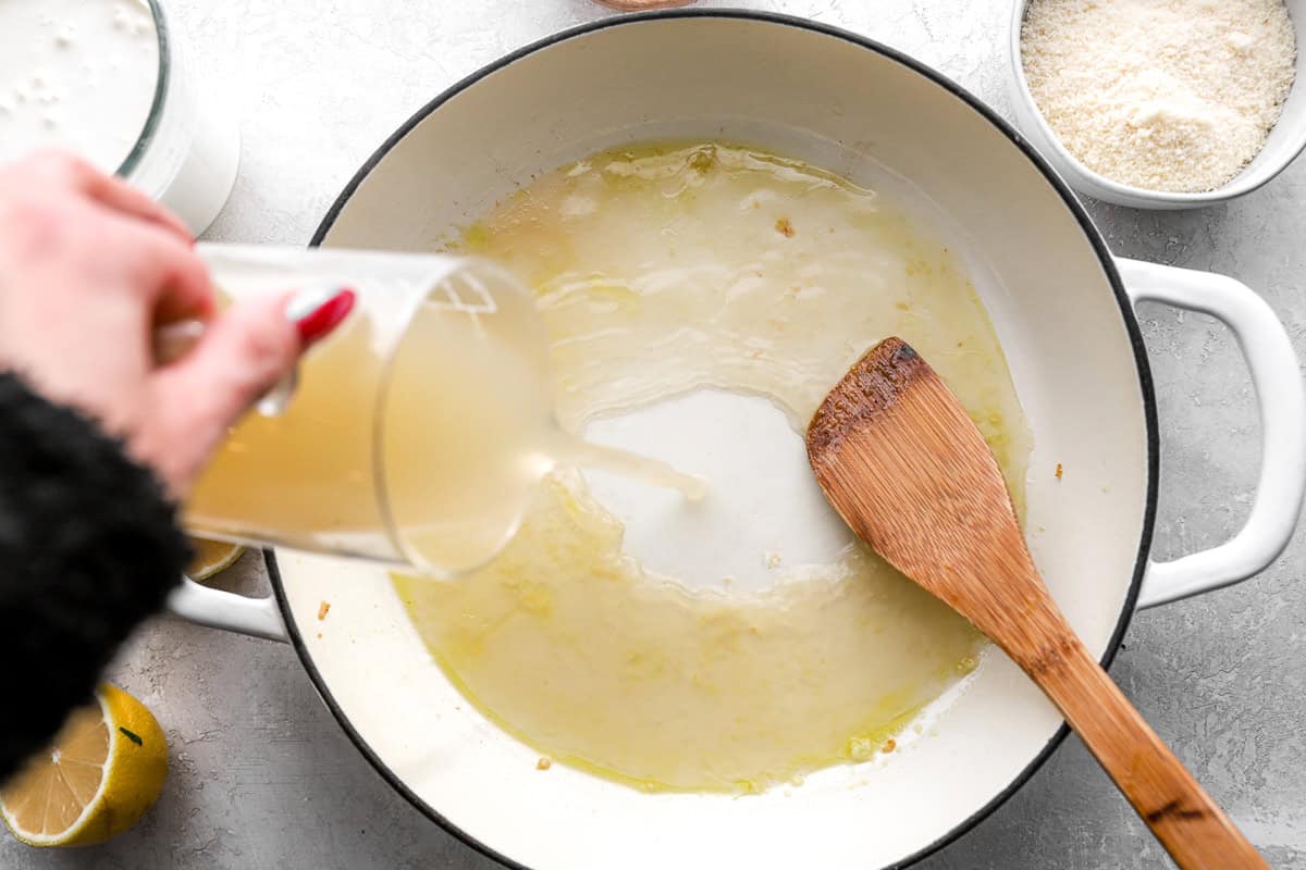 pouring chicken broth into a pan with a wooden spatula.