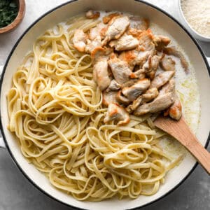 cooked chicken slices and pasta in a pan with alfredo sauce.